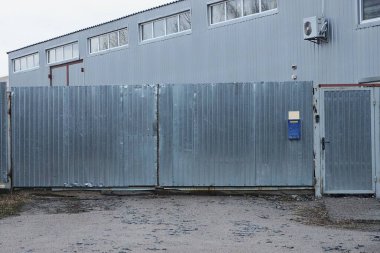 Büyük, gri bir metal kapı ve kırsal sokaktaki çitin bir kısmı.