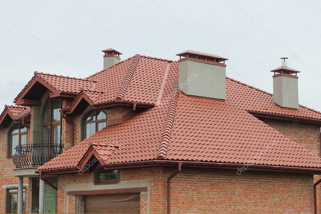 part of a private brick house with an iron balcony under a red tiled roof with concrete chimneys against a gray sky