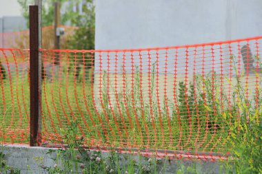 Yeşil çimenlikteki gri beton bir temelde kırmızı plastik ağdan yapılmış dekoratif çitler.