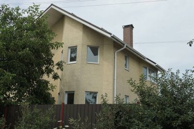 Büyük kahverengi beton tavan arası, dışarıdaki yeşil bitki örtüsünün arkasında pencereleri olan özel bir ev.