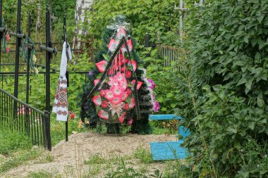 Mezarlıktaki siyah metal bir haçın üzerinde kırmızı yapay çiçeklerle yeşil cenaze çelenkleri.