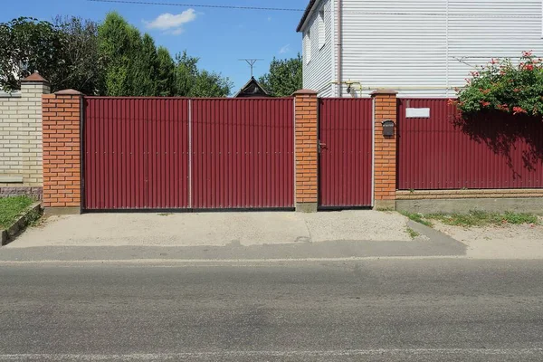 在一条灰色沥青路面上的乡村街道上的铁墙和砖墙上的红色金属门和门 — 图库照片