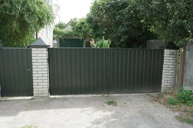 Büyük yeşil bir demir kapı ve sokakta metal ve beyaz tuğlalardan yapılmış bir duvar. 