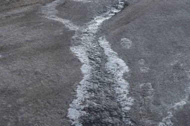 Sokakta donmuş bir derenin buzlu olduğu gri asfalt bir yolun parçası.