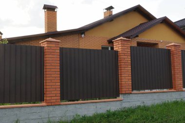  Kahverengi metal ve kırmızı tuğlalardan oluşan bir duvar gri beton bir temel üzerine yeşil çimlerde kırsal bir caddede.