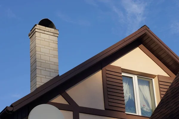 青い空に向かって窓のある民家の茶色い屋根裏部屋に白いレンガの煙突が一つ — ストック写真
