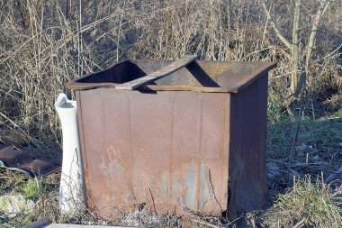 Eski kahverengi paslı bir çöp tenekesi sokakta çimlerin üzerinde duruyor.