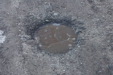 Yolun gri asfaltında buzlu, kahverengi kirli suyu olan bir çukur.