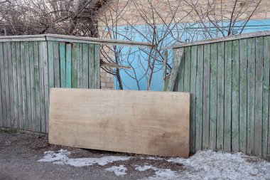 Kırsal bir kış sokağında, beyaz kar altında, kırık, eski, ahşap, gri bir çit duvarının parçası.