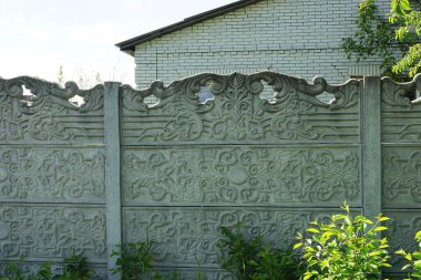 Yeşil bitki örtüsünde, kırsal bir sokakta, uzun, gri beton bir duvarın parçası.