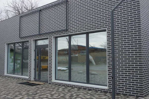 灰色の歩道の近くの通りにガラスのドアと大きな窓のある建物の黒いレンガの壁 — ストック写真