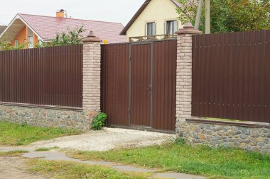 Bir kahverengi metal kapı ve bir taş temelde demir ve tuğladan yapılmış bir çitin parçası.