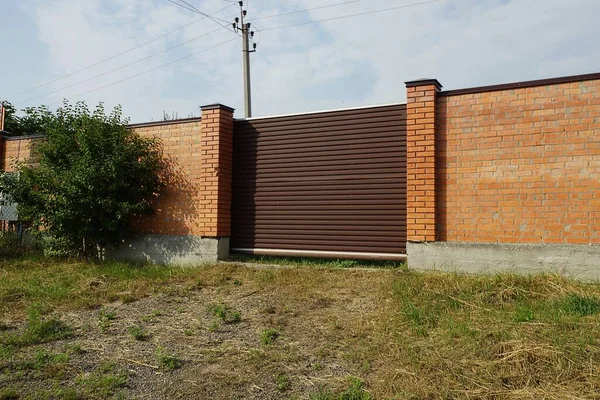 在草地上篱笆的砖墙上的一个棕色金属门 — 图库照片