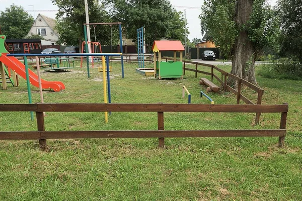 Kahverengi bir ahşap çitin arkasındaki yeşil çimenlikteki oyun alanının bir parçası.