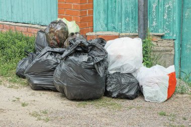 Bir yığın siyah beyaz plastik torba ve çöp yerde yatıyordu. Sokaktaki çitin yanında.