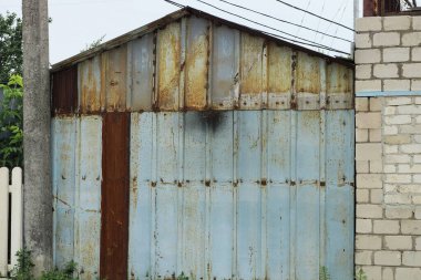 Caddedeki kahverengi pas içindeki eski gri metal bir garajın cephesi.