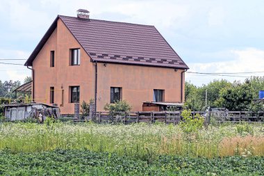 Sokakta yeşil çimenlerin altında fayanslı bir çatı altında pencereleri olan büyük kahverengi bir evin ön cephesi.