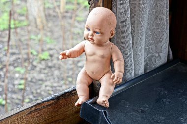 one small brown dirty plastic doll sits on a wooden windowsill near an open window in a room