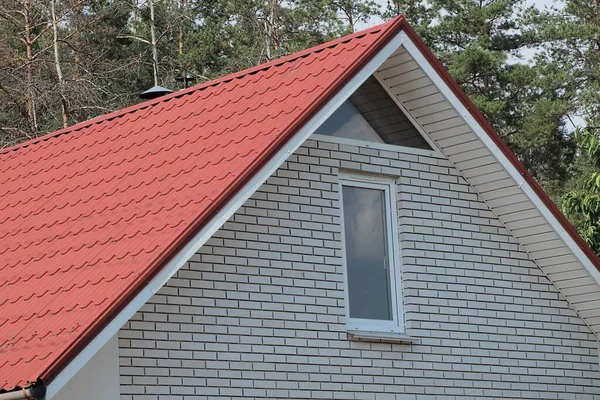 Beyaz tuğlalı tavan arasında, kırmızı kiremitli çatının altında yeşil ağaçların arkasında özel bir evin pencereleri var.