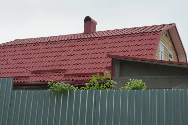 在灰色天空的映衬下 街道上的绿色金属围墙后面 是红色的砖瓦屋顶 有一幢私人住宅的烟囱 — 图库照片