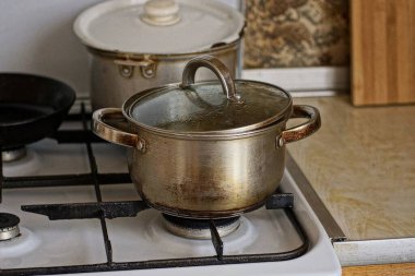 a one gray dirty metal saucepan with a lid on the stove