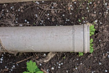 Bir gri plastik boru nemli zeminde ve sokaktaki yeşil çimenlerde yatıyor.