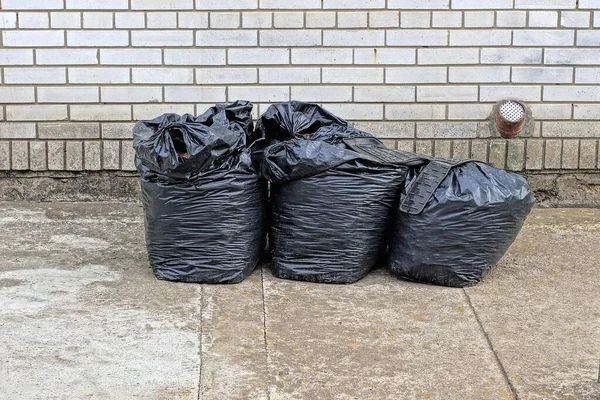 Three Black Full Plastic Garbage Stand Gray Asphalt White Brick — Stock Fotó