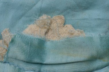 yırtık bir delik ve gri pamuklu kirli mavi kumaştan yapılmış eski bir battaniyenin parçası.