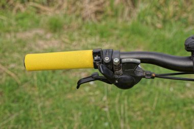 part of a black metal bicycle handlebar with a handbrake and a yellow plastic handle on a background of green grass in nature