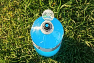 Bir plastik şişe mavi içecekle yeşil çimlerde duruyor.