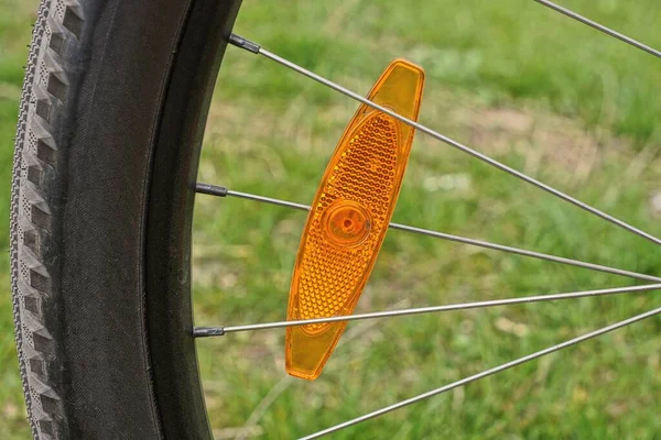 一辆黑色自行车轮子灰色金属轮轴上的红色塑料反射镜映衬在自然界绿草的背景下 — 图库照片