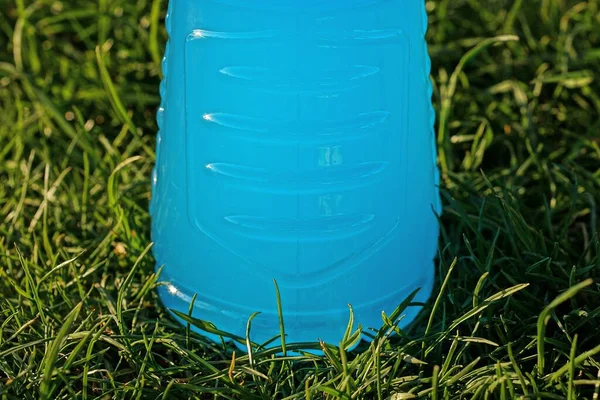 一个装有蓝色饮料的塑料瓶屹立在自然界的青草中 — 图库照片