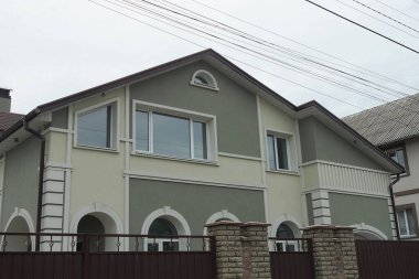 Sokakta gri bir gökyüzüne karşı kahverengi çitlerin arkasında pencereleri olan büyük yeşil bir evin ön cephesi.