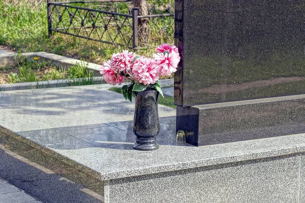 Mezarlıktaki bir mezarın üzerindeki granit bir anıtta kırmızı çiçekli siyah bir mermer vazo.
