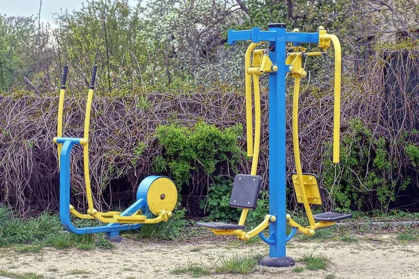 公園の緑の植生の近くの灰色の砂の中に2つの金属製の青い黄色のスポーツ用具が立っています — ストック写真