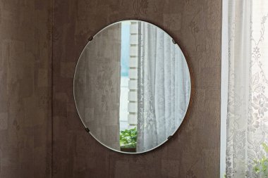 one large round glass mirror with reflection hangs on a brown wall in the room clipart