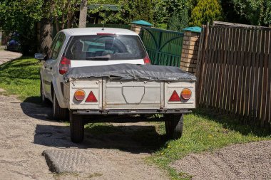 Siyah brandayla kaplı gri bir römorku olan bir araba çitin yanındaki sokakta duruyor.