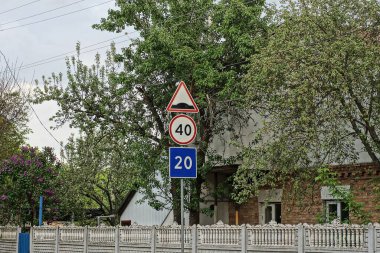 Üç yol işareti hız sınırı ve beton çitin yanındaki demir bir direkte hız tümseği.