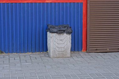 Bir gri beton kutu dışarıda kaldırımda duruyor. Mavi ve kahverengi metal bir duvara karşı. 