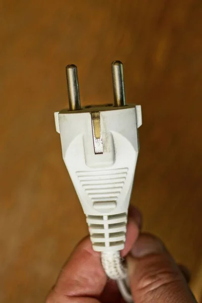 手拿着白色旧插座的手指 插座上有棕色背景的电缆 — 图库照片