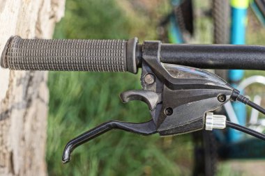 Siyah metal bir gidonun parçası. Plastik saplı ve frenli. Sokakta kablo var.