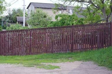 Çitin uzun kahverengi duvarının bir kısmı, yeşil çimlerin içinde, ahşap tahtalardan yapılmıştır.
