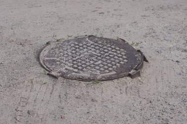 Caddedeki gri kumların üzerinde kahverengi metal bir lağım çukuru var.