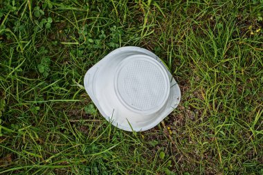 Beyaz plastik bir tabaktan çıkan çöp doğadaki yeşil çimlerin üzerinde yatıyor.