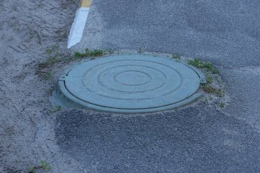 Gri asfalt yolda çimenlerdeki eski yeşil demir lağım çukuru.
