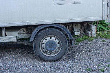 Büyük kirli siyah bir tekerlek beyaz bir kamyonun üzerinde duruyor gri asfalt üzerinde