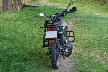 Sokakta yeşil çimlerin üzerinde büyük siyah bir motosiklet duruyor.