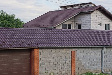 Kahverengi kiremitli çatının altında kapısı olan uzun gri tuğla bir duvar.