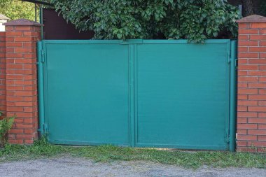 Bir yeşil kırsal demir kapı, caddedeki kırmızı tuğlalı duvarın kapalı kapısı.