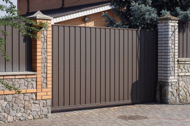 Büyük, kapalı, kahverengi bir kapı. Tuğladan bir duvarın üzerinde. Gri bir kaldırımın üzerinde.